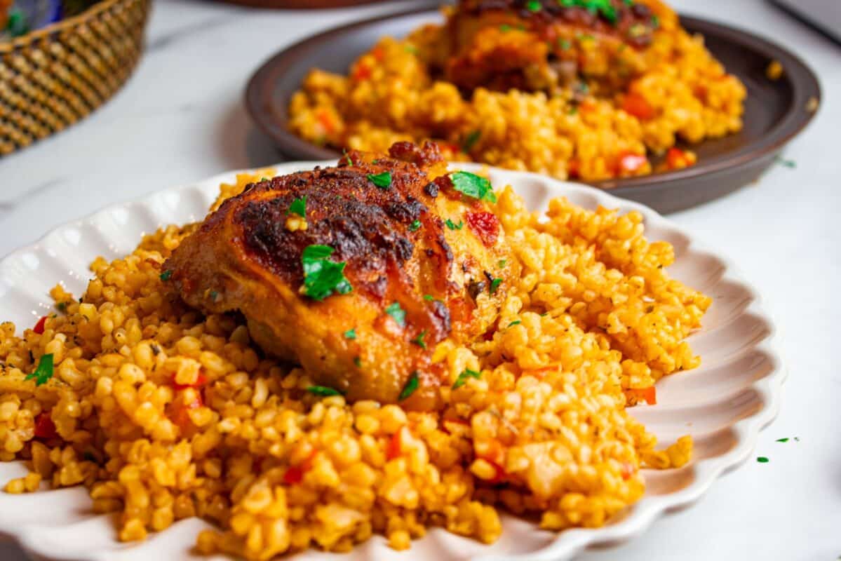 roast garlic harissa chicken served on top of two plates of Turkish bulgur pilaf and garnished with finely chopped fresh parsley