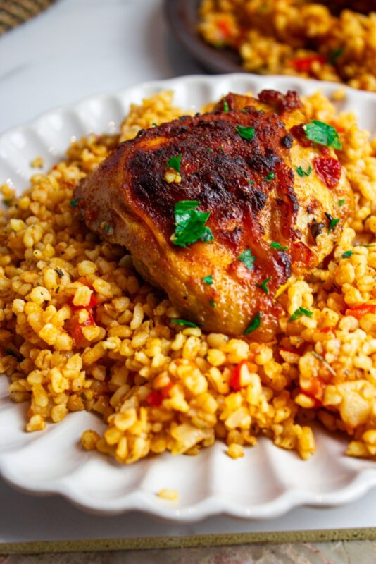 a plate of bulgur and tomatoes pilaf served with garlic harissa chicken