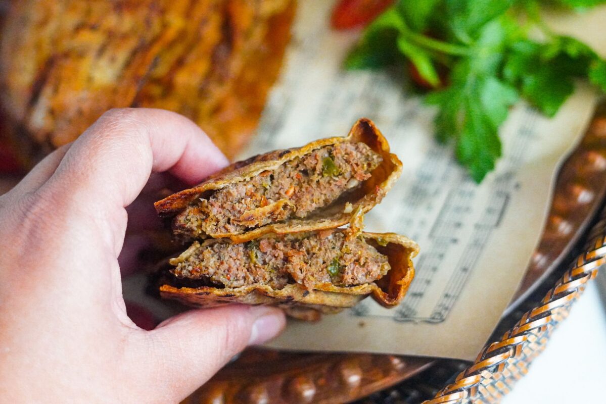 A hand holding 2 juicy golden crispy pockets low carb arayes of ground beef stuffed pitas. 
