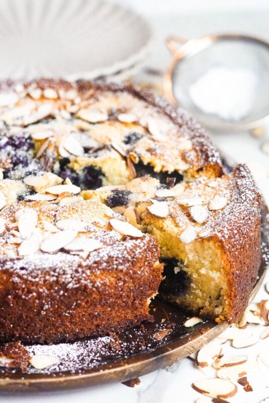 a golden baked cake with ricotta and frozen blueberries, garnished with almonds and dusted sugar