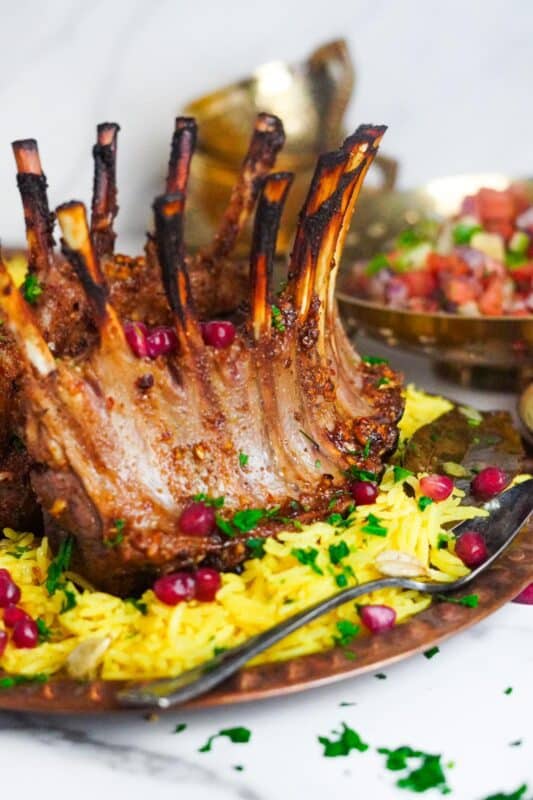 A flavorful pomegranate lamb and saffron rice meal in a copper plate, with a bowl of salad in the background