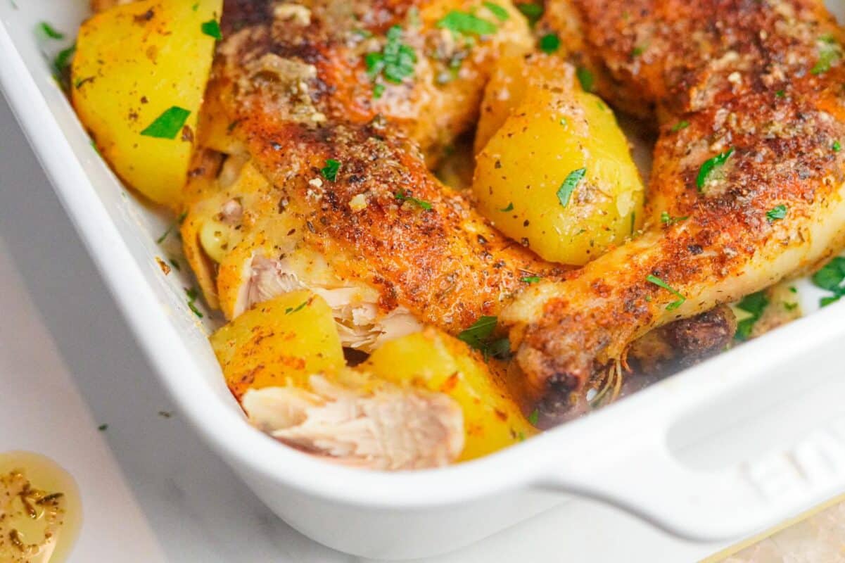 a close shot of a sheet pan of crispy Greek-style baked chicken and potatoes garnished with chopped fresh parsley