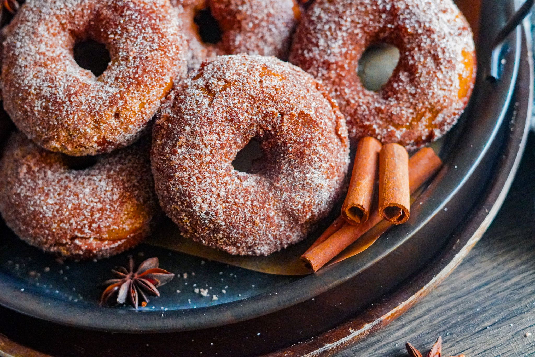 homemade donuts made with pumpkin with cinnamon sugar coating, next to them cinnamon sticks