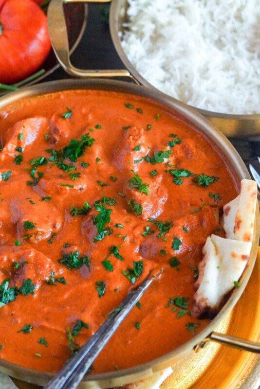 creamy chicken tikka masala served with white rice, naan bread, and finely chopped parsley on top