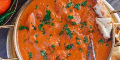 A dish of creamy, tomato-based chicken tikka masala dish with marinated chicken pieces, rich in Indian flavor. It is garnished with some parsley and set with traditional Indian naan.