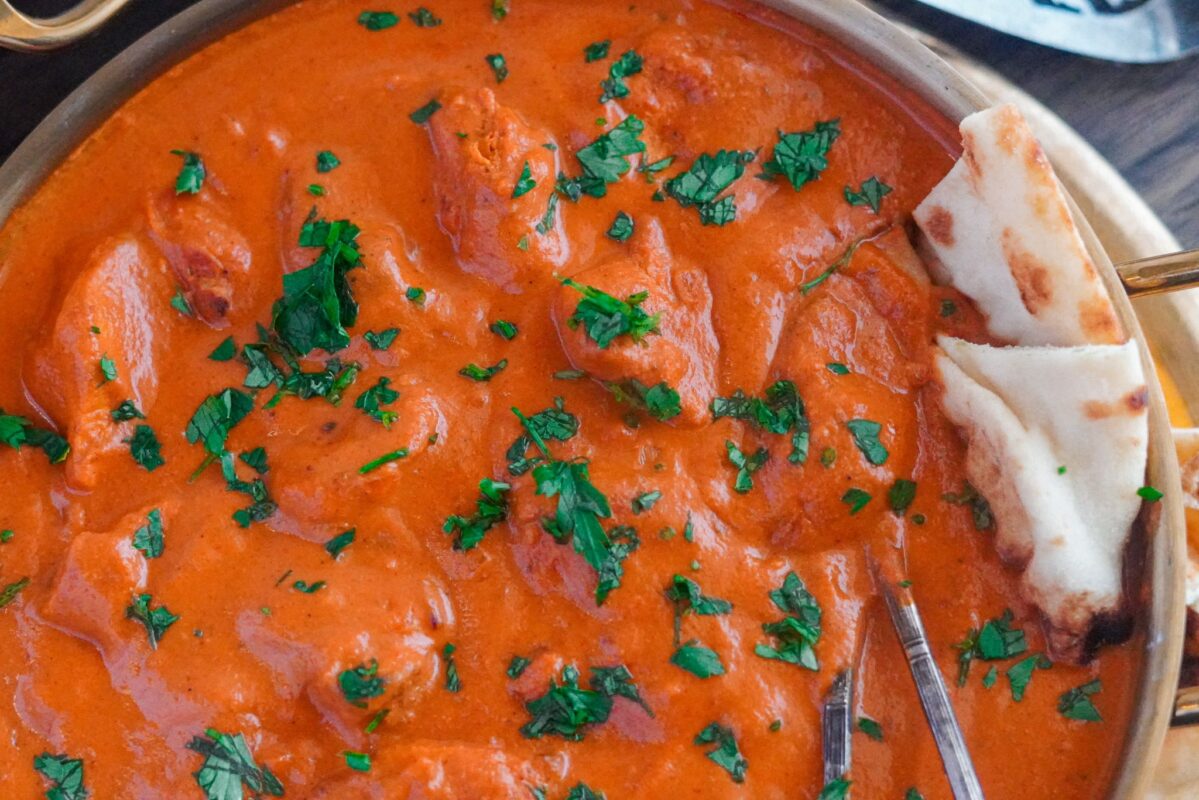 Chicken Tikka Masala is a creamy, tomato-based dish with marinated chicken pieces, rich in Indian flavor. It is garnished with some parsley and set with traditional Indian naan.