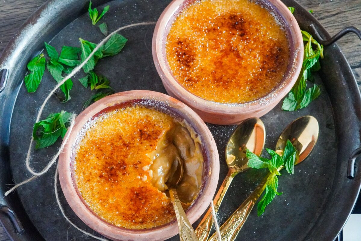 two bowls of golden pumpkin brulé on a tray with a few spoons and fresh mint next to them