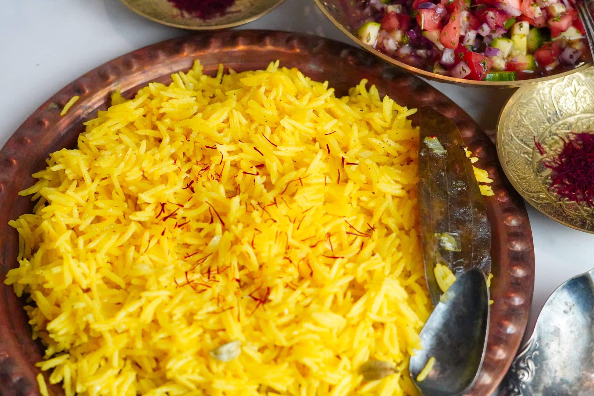 Yellow saffron rice, garnished with vibrant red saffron threads is set within fancy, traditional copper plates with a salad on the side.