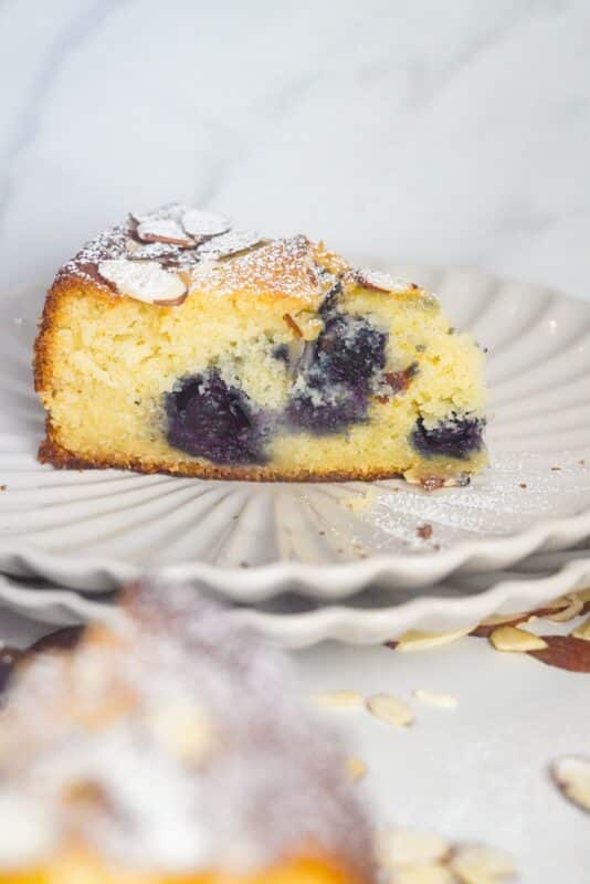 A single slice of almond ricotta cake filled with frozen blueberries, elegantly presented on a white plate