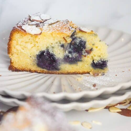 A blueberry almond ricotta cake, shaped like a triangle, is placed on a white plate.
