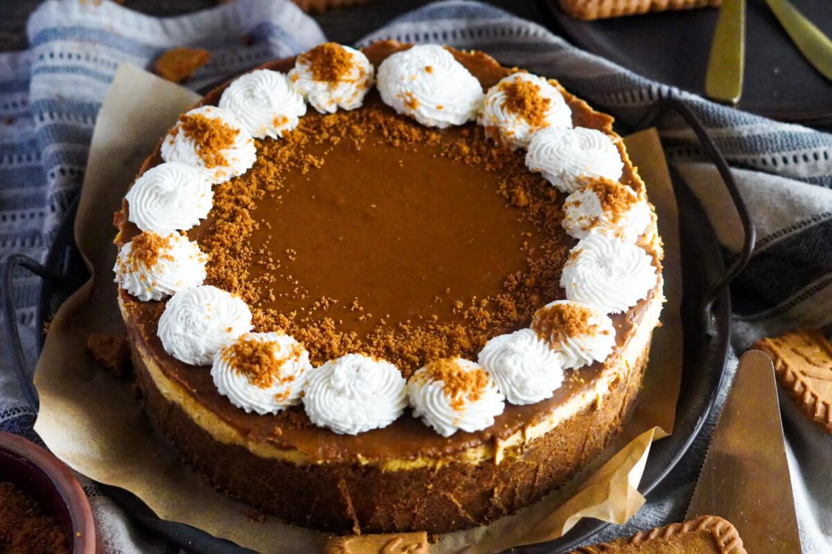 This image shows Biscoff and pumpkin cheesecake, perfectly glazed with Biscoff spread, dusted with biscoff cookie crumbles, and decorated with perfect balls of whipped cream.