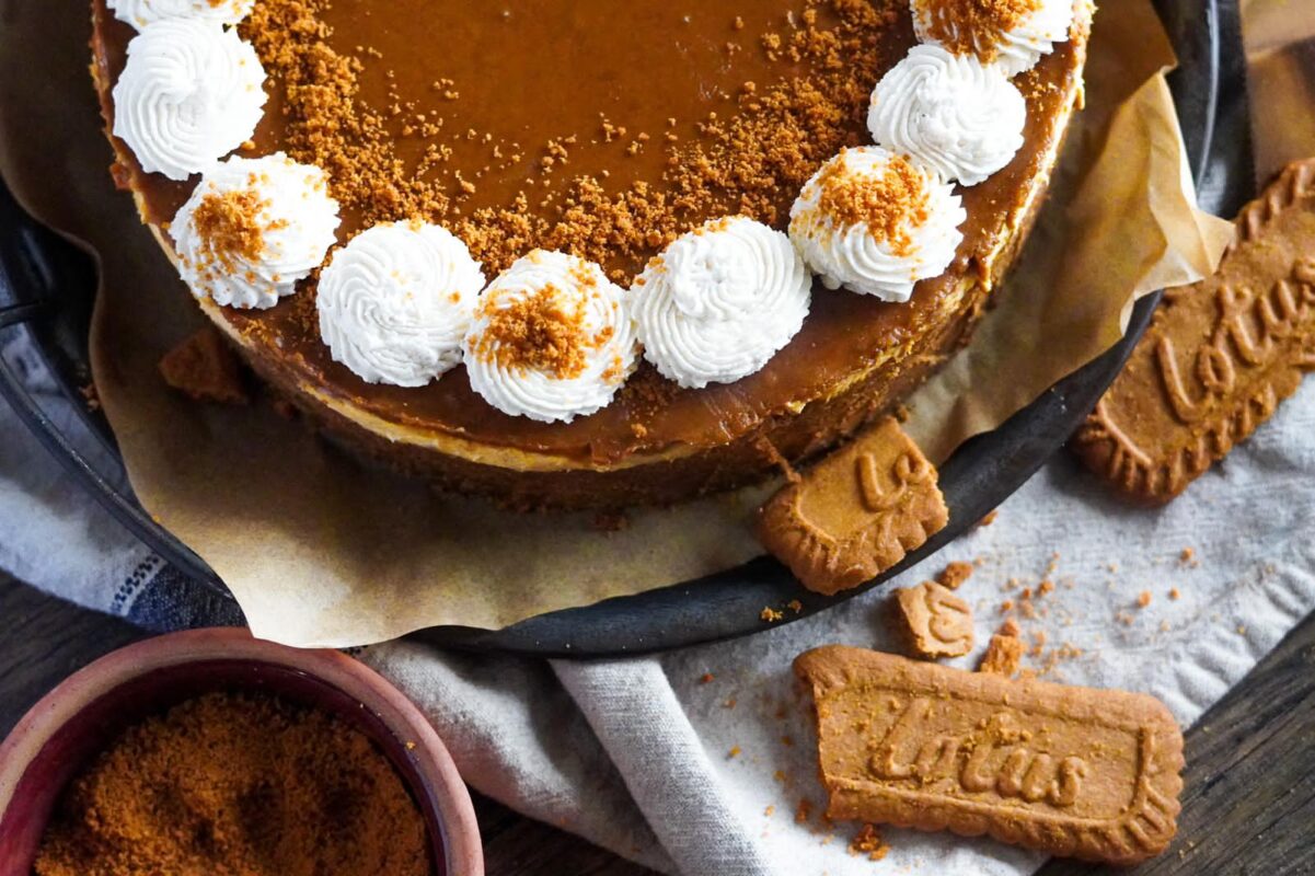 This image shows Biscoff and pumpkin cheesecake, perfectly glazed with Biscoff spread, dusted with biscoff cookie crumbles, and decorated with perfect balls of whipped cream.