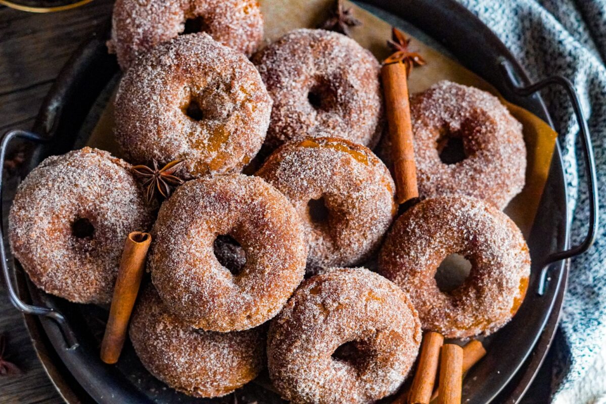 Irresistible pumpkin donuts with sugar coating placed on a tray with star anise and cinnamon sticks
