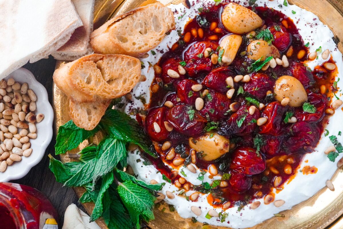 A gold plate of Labneh with spicy confit tomatoes, fresh mint leaves on the side and three toasted bread circles.