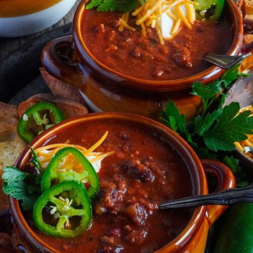 Two bowls of rich thick flavorful chili served with green peppers.