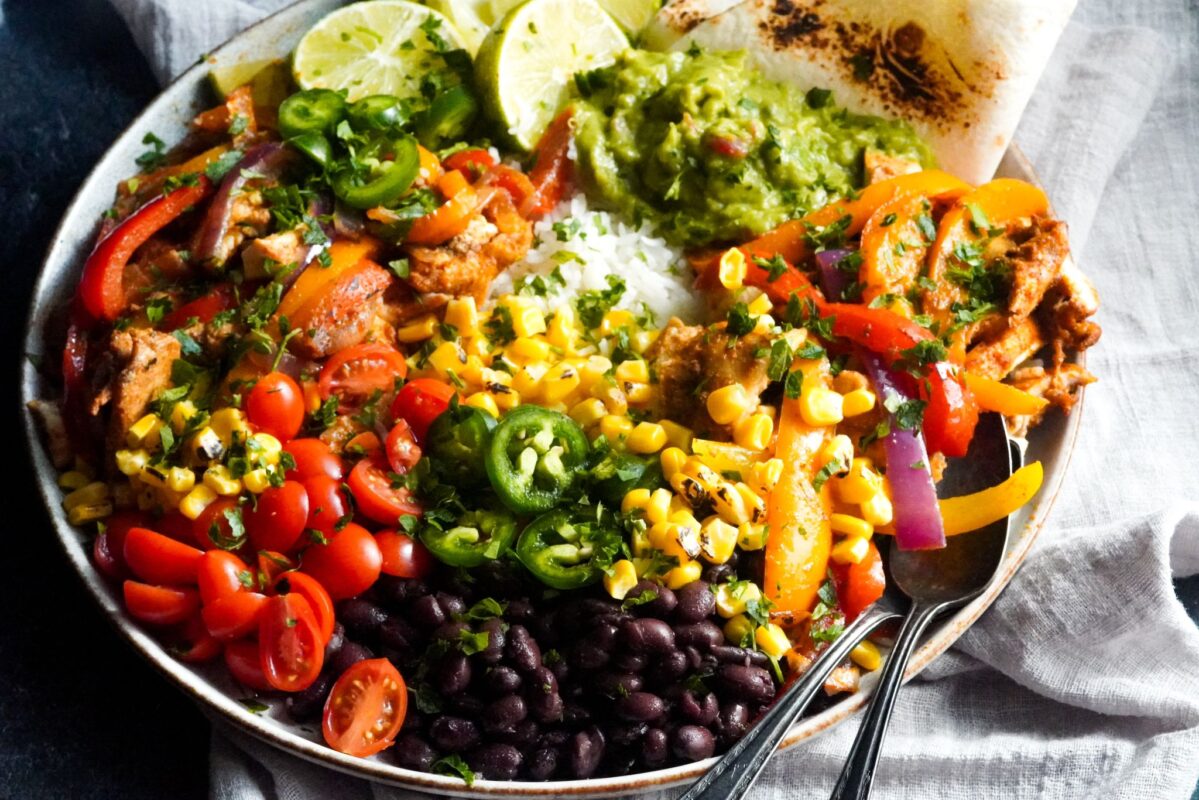best chicken fajitas with rice in a bowl with fresh veggies toppings like tomatoes, peppers, and corn with black beans and guacamole
