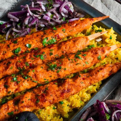 four chicken kafta skewers sprinkled with finely chopped parsley and served with sumac onion salad on a bed of yellow rice