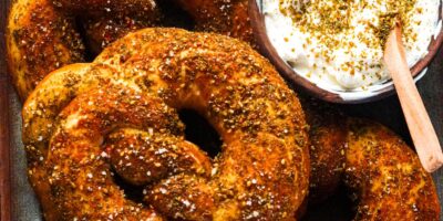 A golden-brown zaatar pretzels sprinkled with flakey salt alongside a bowl of labneh.