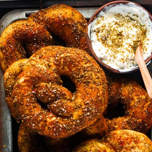 A golden-brown zaatar pretzels sprinkled with flakey salt alongside a bowl of labneh.