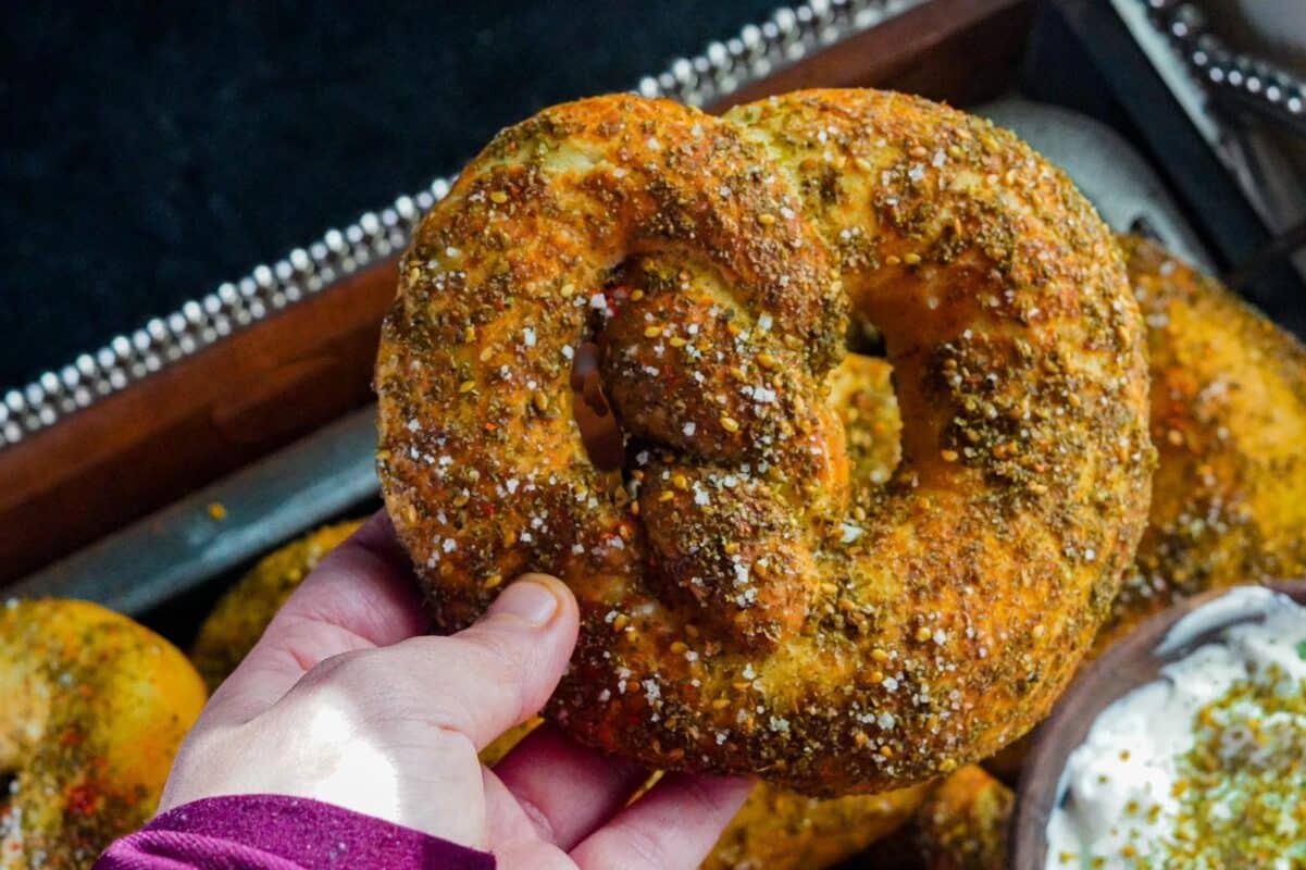 A person is holding one baked zaatar pretzel that's sprinkled with zaatar and flakey salt.