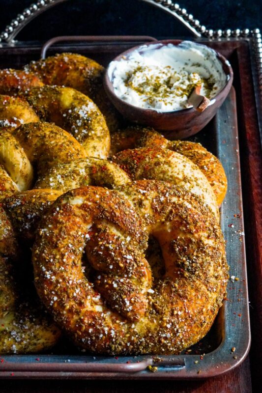 Golden-brown baked zaatar pretzels are sprinkled with zaatar and flakey salt and placed on a tray alongside a bowl of Labneh. 