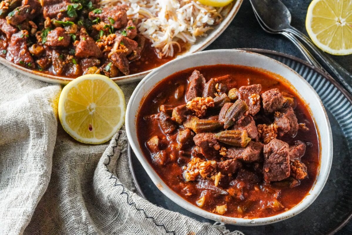 a bowl of bamya stew with beef and a slice of lemon on the side.