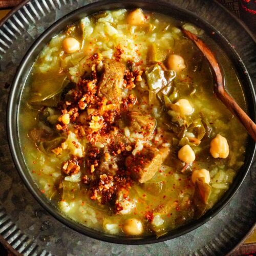 a bowl filled with Fogaiyya stew with beef chunks, Swiss chard, rice, chickpeas, and topped with shatta.