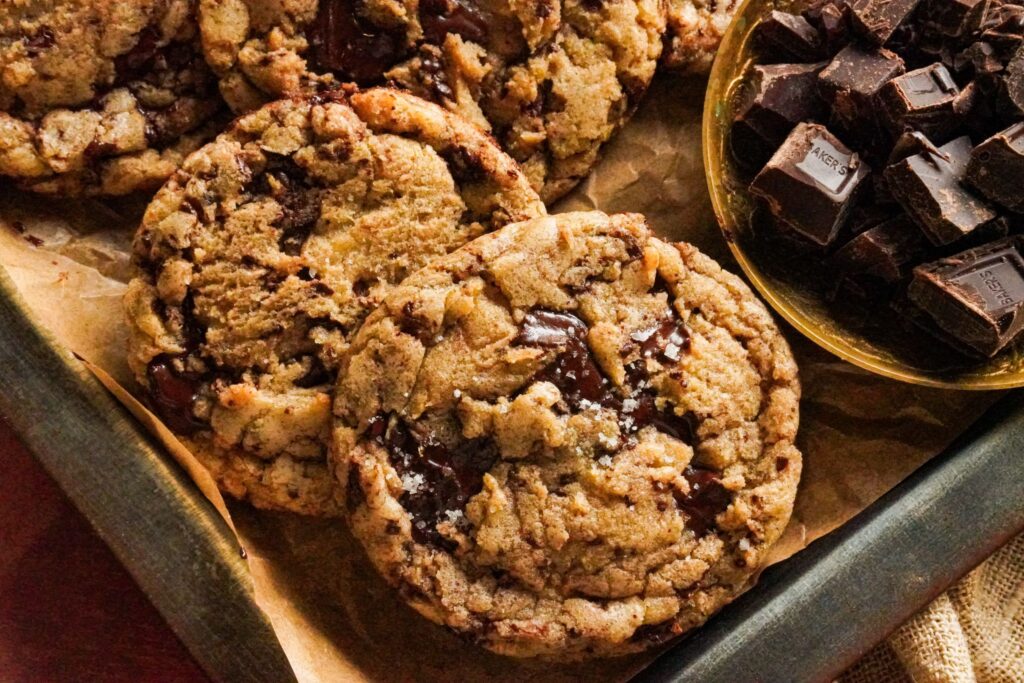 A tray packed with delicious brown butter chocolate chip cookies topped with sea salt, with some chocolate chunks on the side.