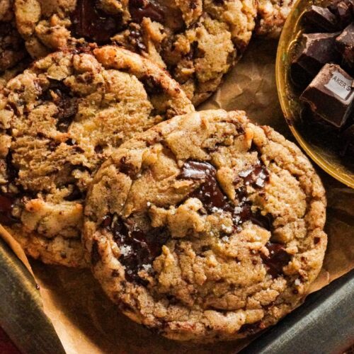 A tray packed with delicious brown butter chocolate chip cookies topped with sea salt, with some chocolate chunks on the side.