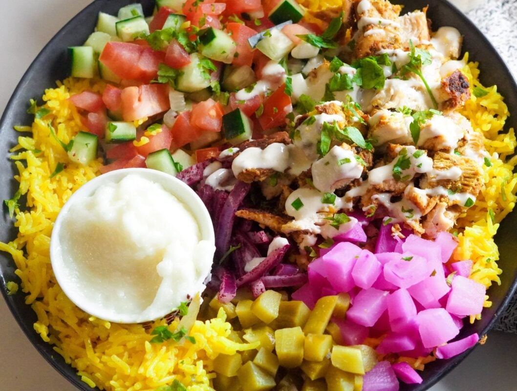 Delicious rice and chicken shawarma bowls are served with toppings of pickles, salad, and white sauce.