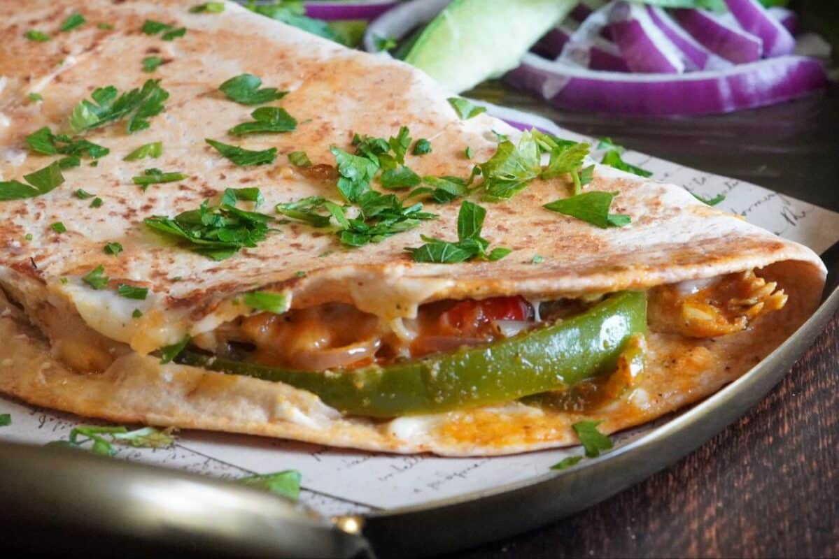 Delicious chicken fajita tortilla wrap with a lot of melted cheese and some parsley on top with fresh vegetables
