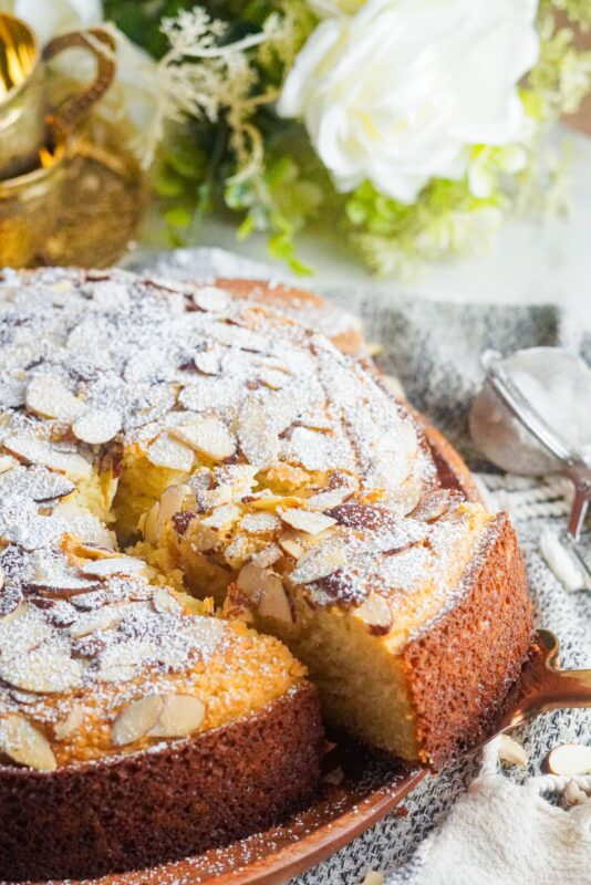 A slice of almond cake topped with sliced almonds and dusted with powdered sugar