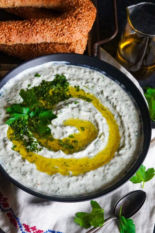 A bowl of hedge mustard and yogurt with a generous drizzle of extra virgin olive oil topped with finely chopped parsley and served with Palestinian sesame bread 