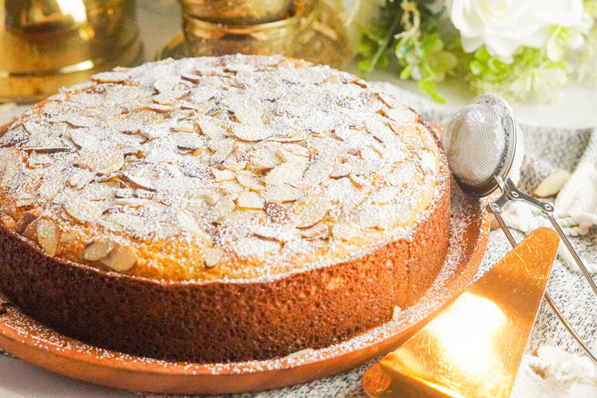 A well decorated almond cake topped with sliced almonds and dusted with powdered sugar