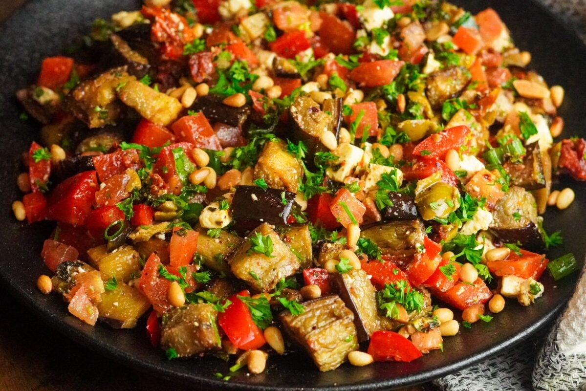 Easy Roasted Eggplant Salad Recipe roasted eggplant salad in a bowl made with roasted eggplants, parsley, olives, tomatoes, green onions, and green bell pepper and seasoned with a savory dressing of pomegranate molasses, olive oil, black pepper, and Aleppo pepper