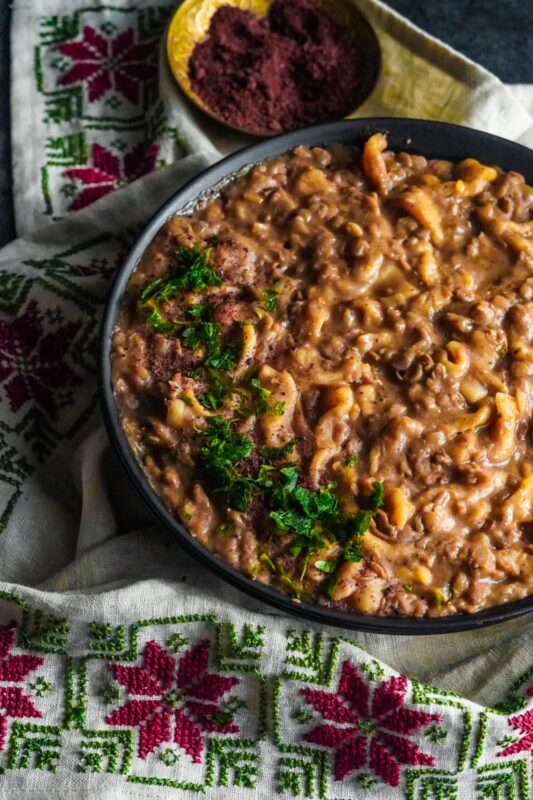 A bowl of authentic Palestinian rashta featuring homemade noodles and brown lentils garnished with chopped parsley