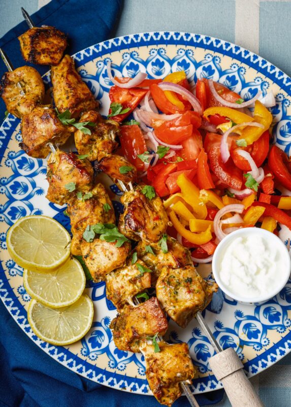 a plate of two skewers of Middle Eastern shish tawook sprinkled with finely chopped parsley served with Arabic chopped salad, a small bowl of garlic sauce, and lemon wedges