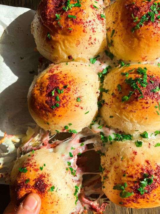 Two rows of toasted sliders line up connected with each other. They are stuffed with chicken musakhan filling and melting mozzarella cheese.