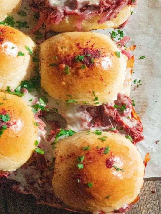 A group of buns line up a tray while some molten mozzarella steps out. The buns contain chicken musakhan and are topped with sumac.