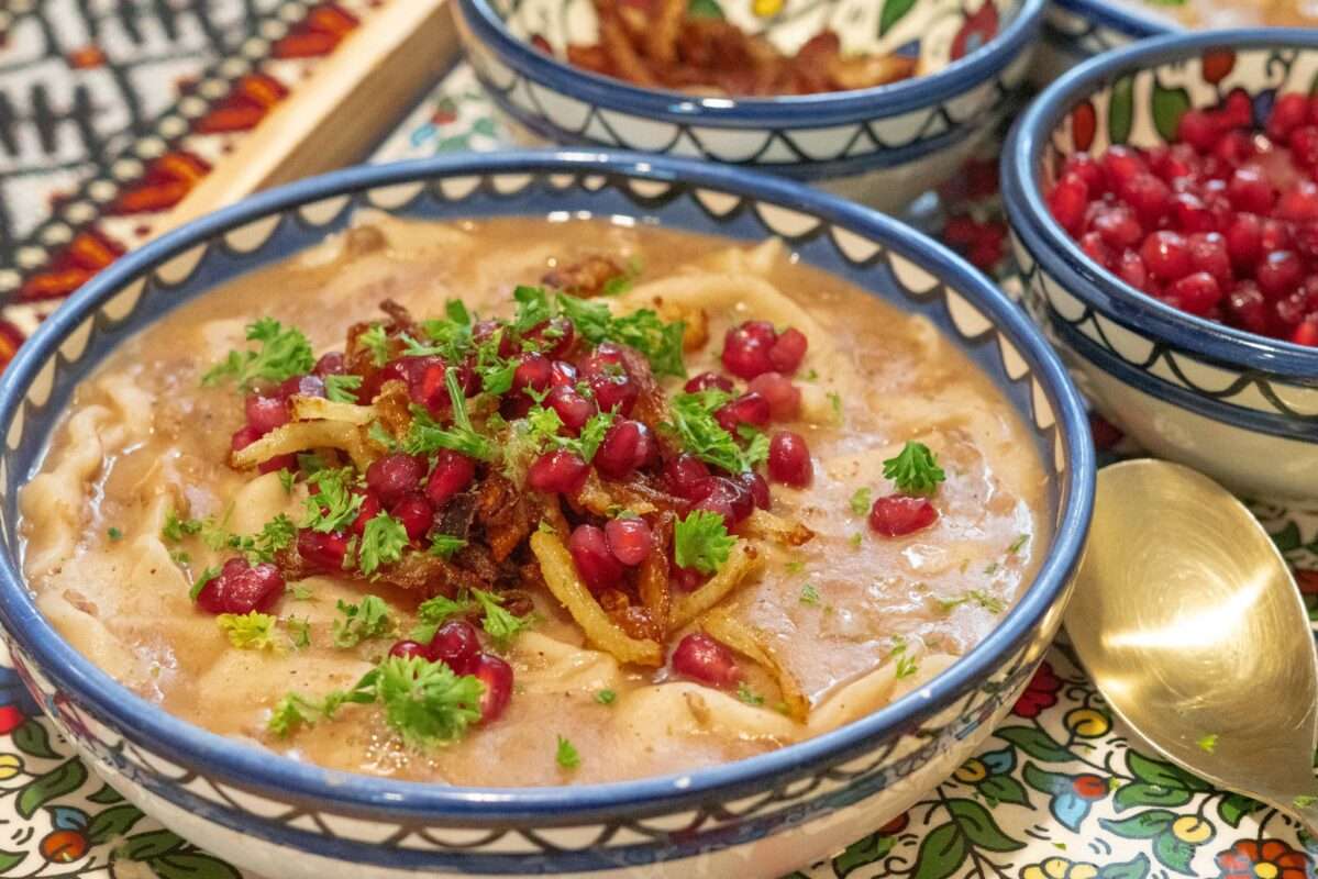 a bowl of warm Rashta topped with caramelized onions, parsley and pomegranate 