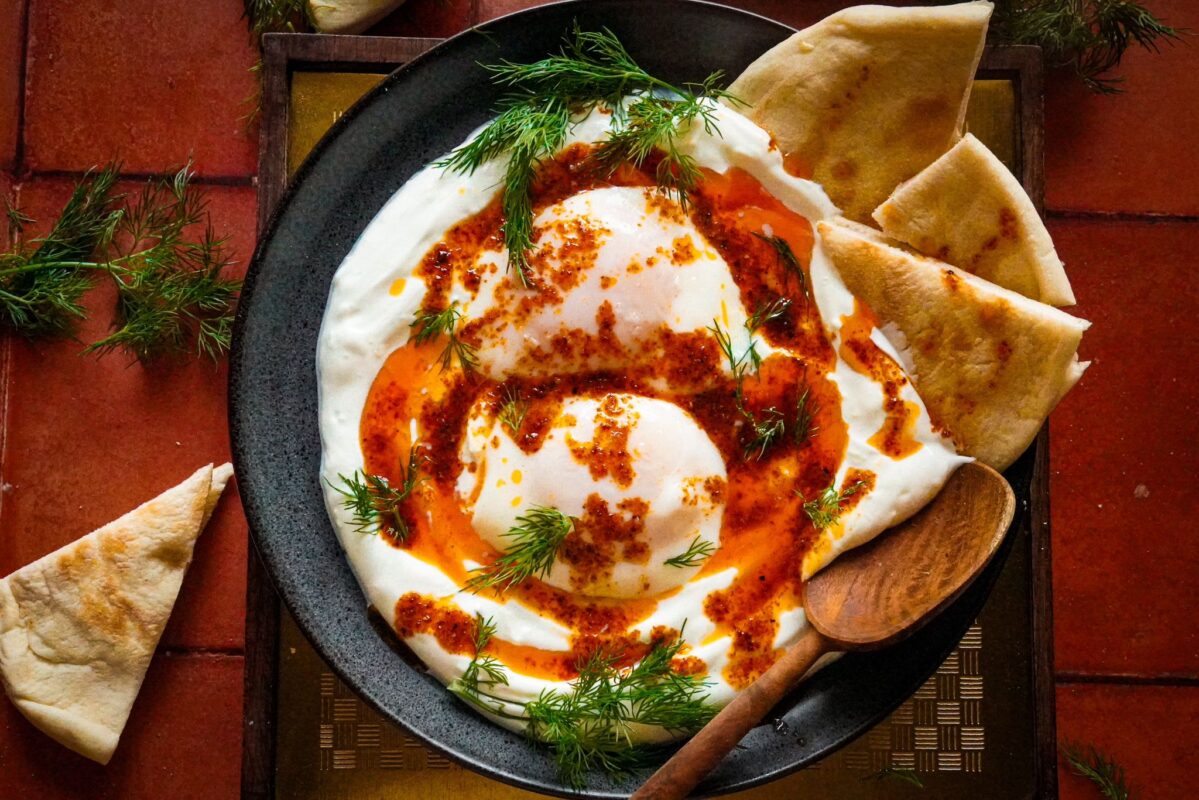 a top view of a plate of Turkish eggs bathed in an Aleppo garlic butter sauce and sprinkled with a generous amount of chopped fresh dill and served with pita bread