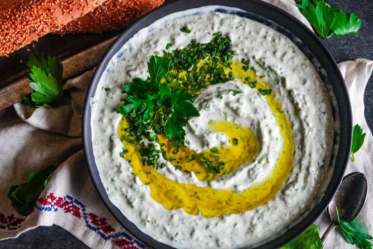 A top view of a bowl of hedge mustard and yogurt with a generous drizzle of extra virgin olive oil topped with finely chopped parsley and served with Palestinian sesame bread