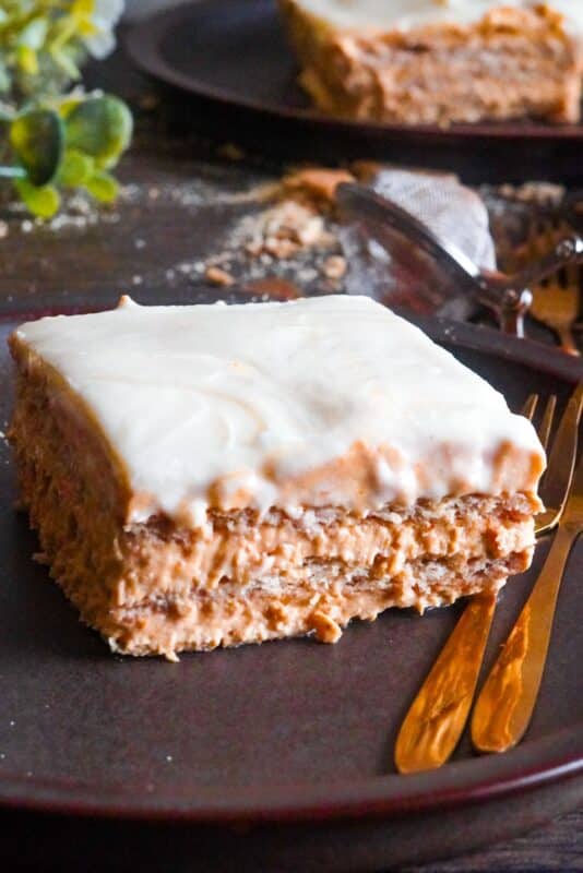 A close-up of a slice, showcasing creamy layers of vanilla frosting, graham crackers, and pumpkin puree.