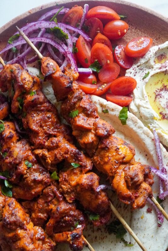 A plate full of golden chicken skewers with side of onions and cherry tomatoes.