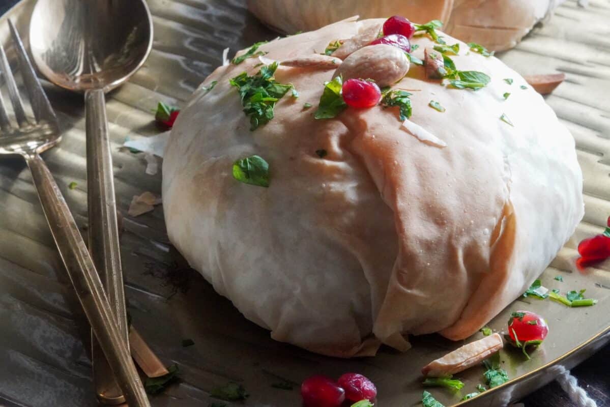 Middle Eastern Beef Ouzi Pockts Crispy phillo is filled with a hearty mix of nuts and rice. It is served with finely chopped fresh parsley, fresh pomegranate seeds, and toasted nuts.