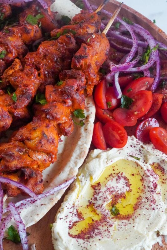 A big portion of hummus mtabal with chicken skewers and cherry tomatoes.