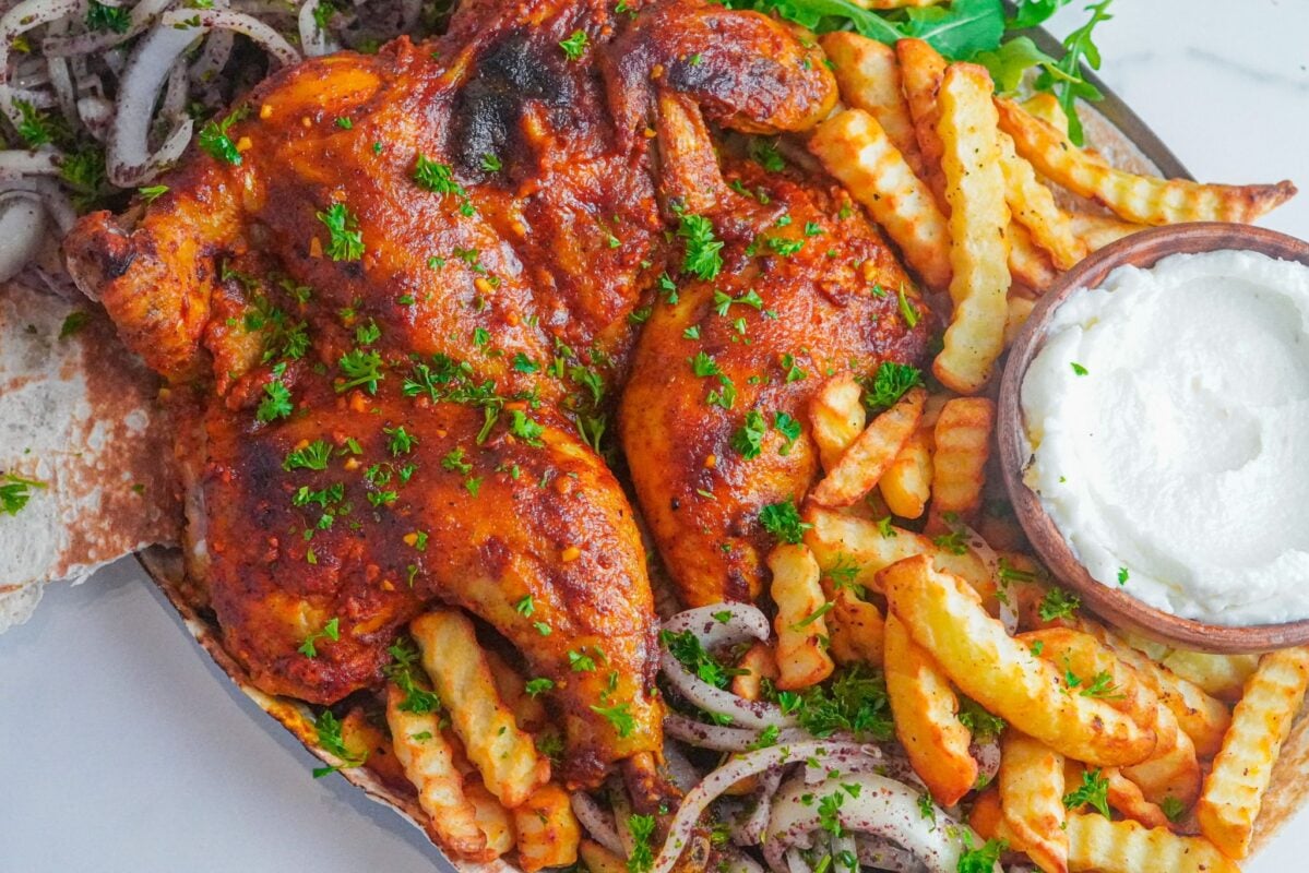A baked to perfection chicken with crinkle-cut fries and garlic paste on the side, accompanied with onion and sumac salad.