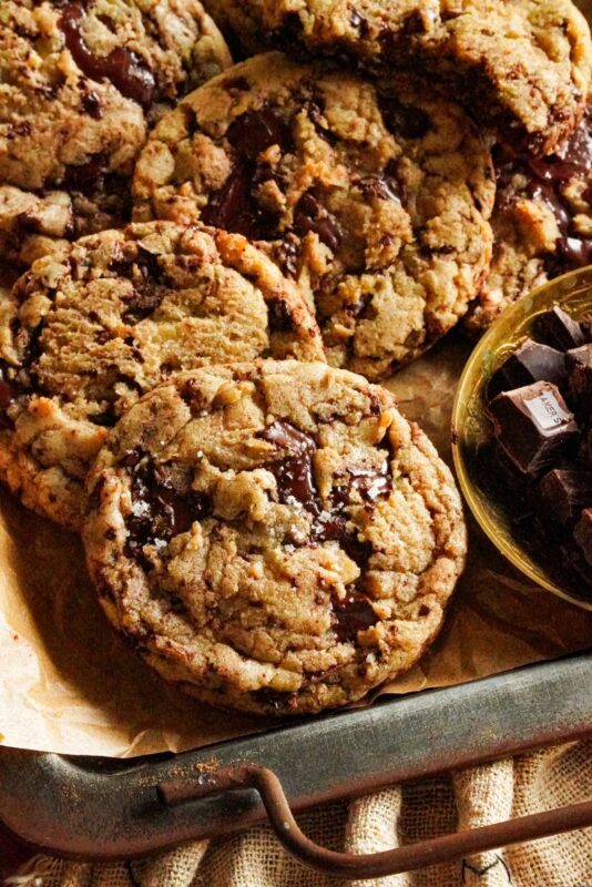 A tray packed with delicious brown butter chocolate chip cookies topped with sea salt, with some chocolate chunks on the side.