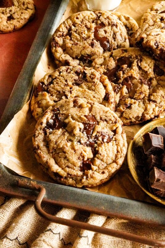 A tray packed with delicious brown butter chocolate chip cookies topped with sea salt, with some chocolate chunks on the side.