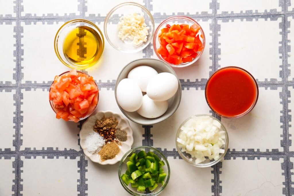 Shakshuka ingredients: eggs, chopped onion, minced garlic, diced tomatoes, diced bell pepper, olive oil, spices, and tomato sauce